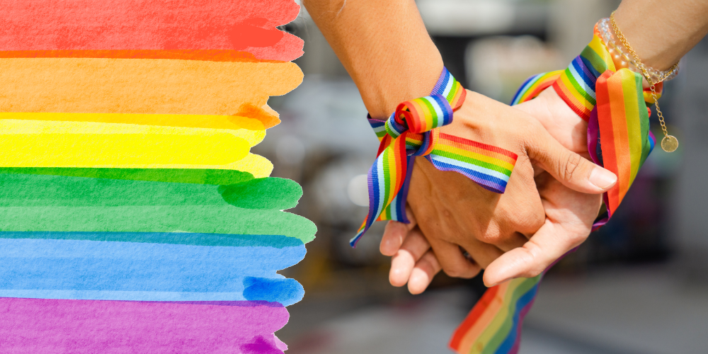 Close-up on holding hands wearing rainbow bracelets and ribbons.