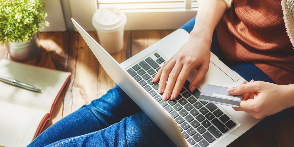 A laptop computer in a woman's lap. She is holding a credit card to make a purchase online.