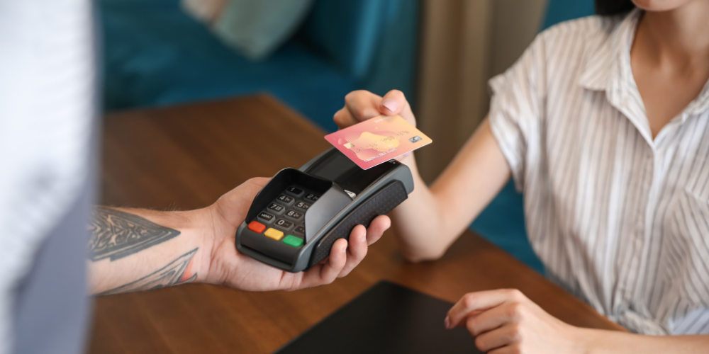 A woman sitting at a restaurant table taps her card to pay on a mobile card reader.