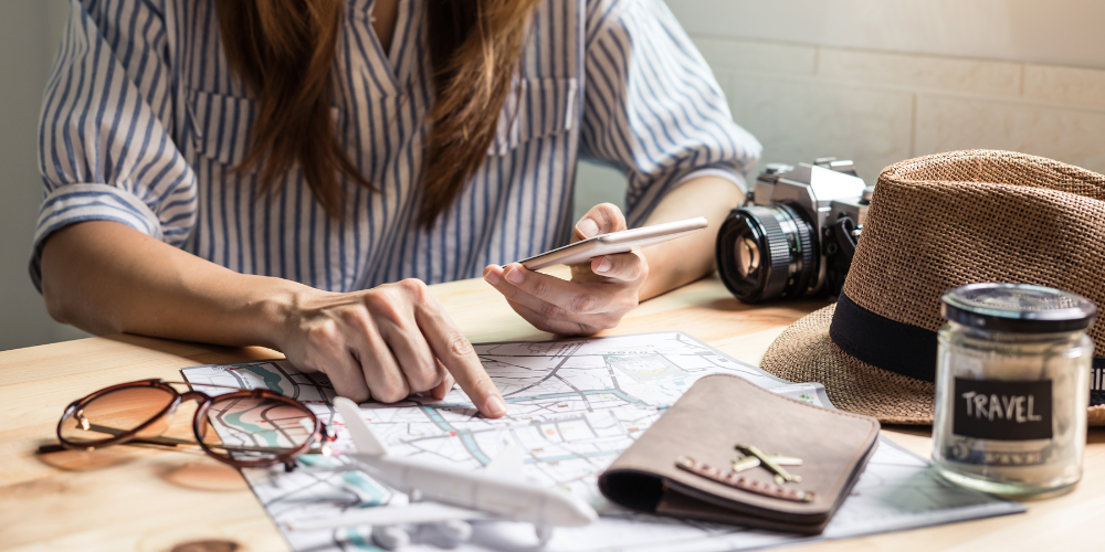 A woman is planning a trip using her phone, a map, and her budget in a jar.