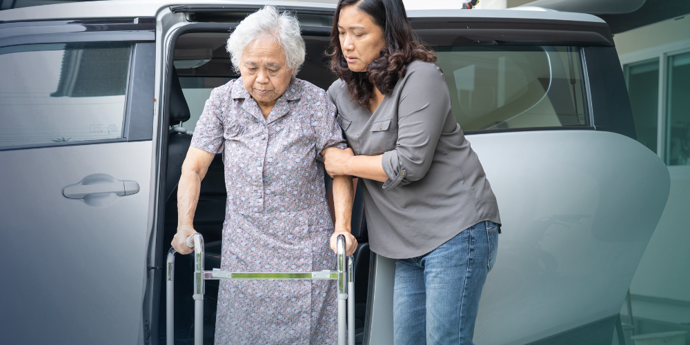 A woman helps support an eldery woman using a walker