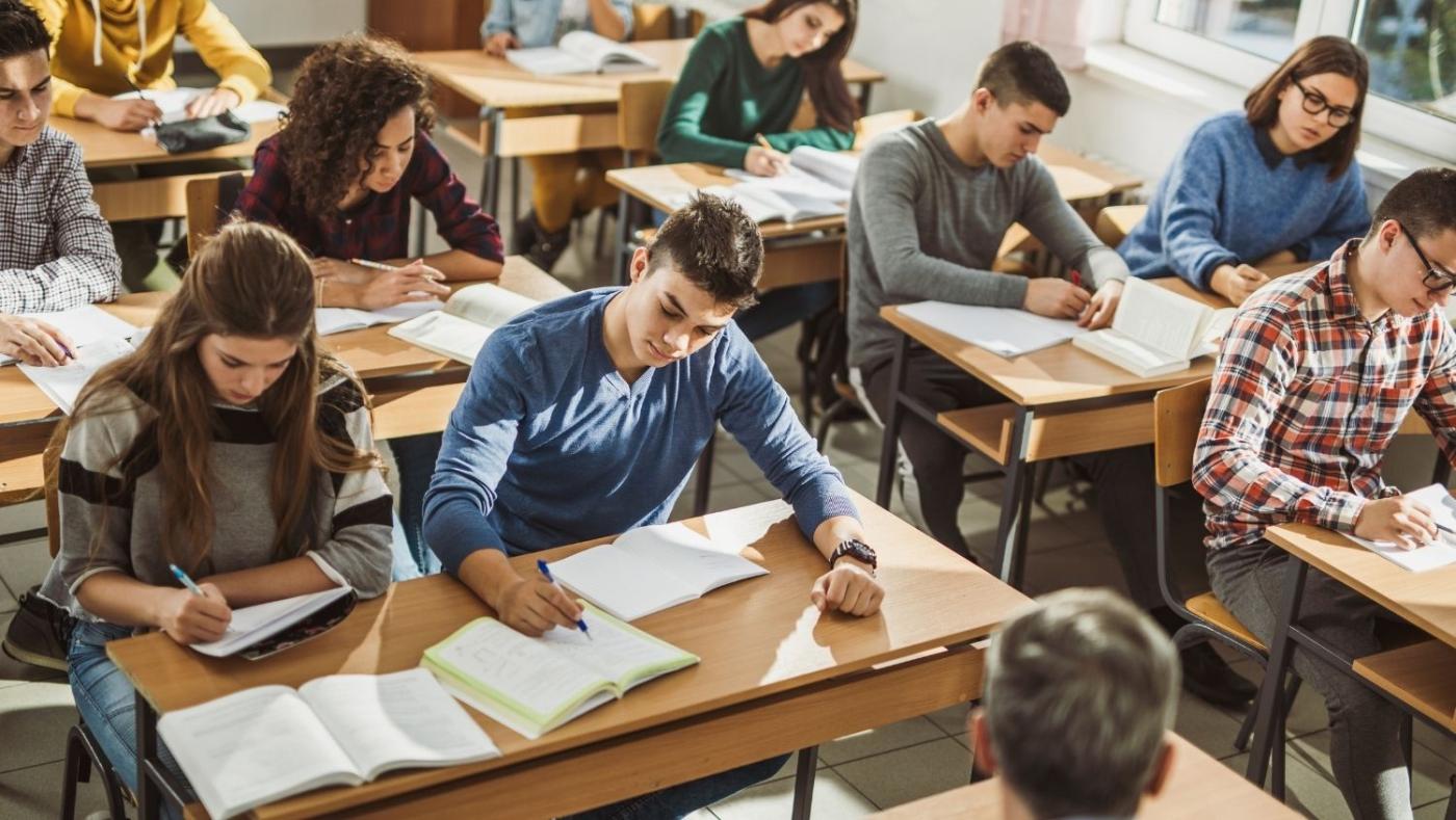 Alumnos en un salón de clases, escribiendo en sus cuadernos. 