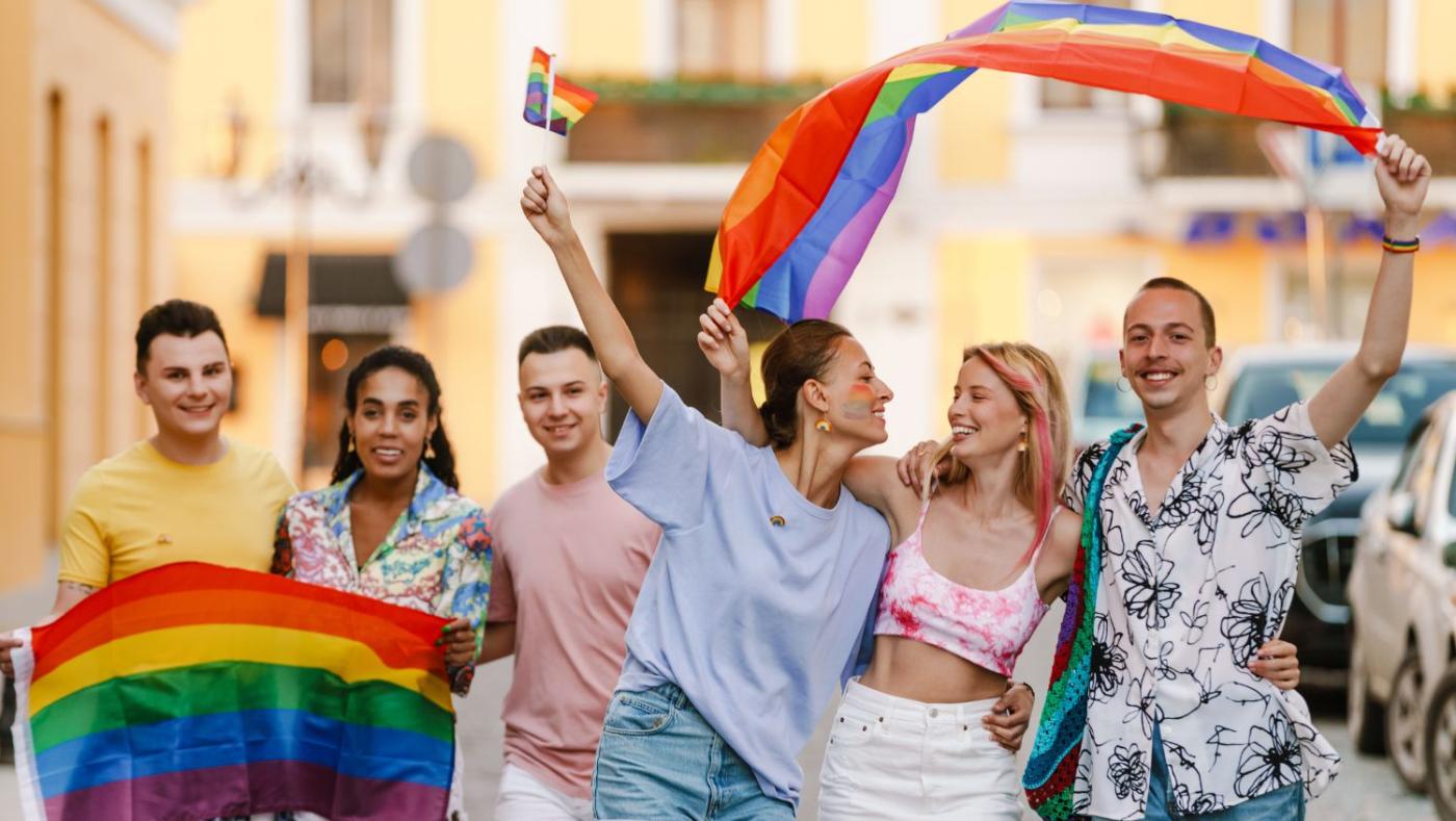 Personas jóvenes con banderas arcoiris celebrando el mes del orgullo.