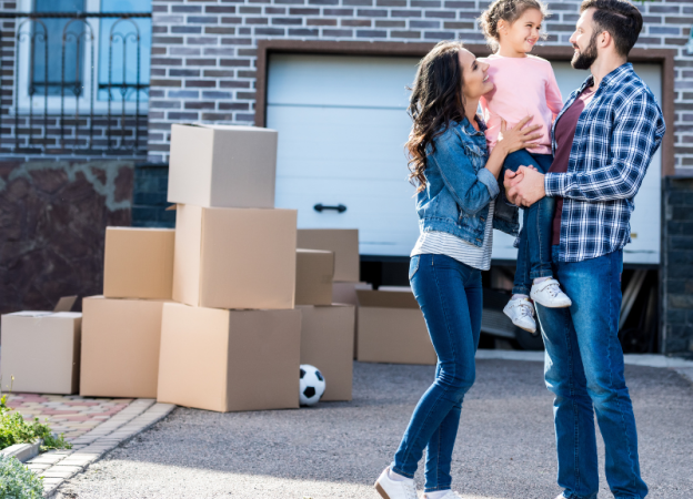 A family stands outside of their new home, with moving boxes in the background.
