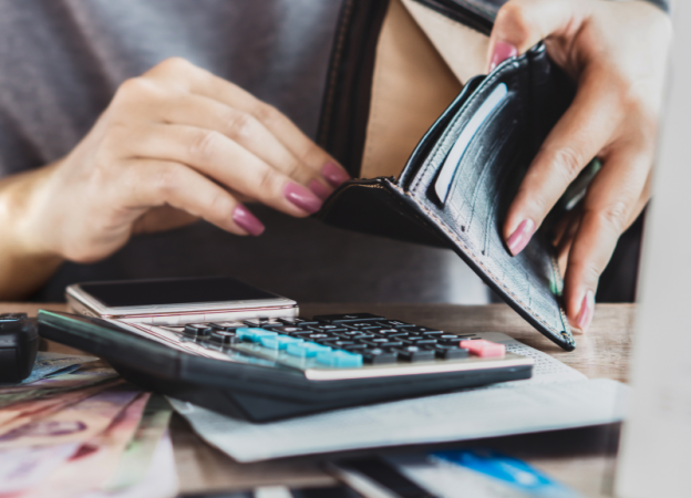 A woman checks her wallet for cash while doing her budget with a calculator