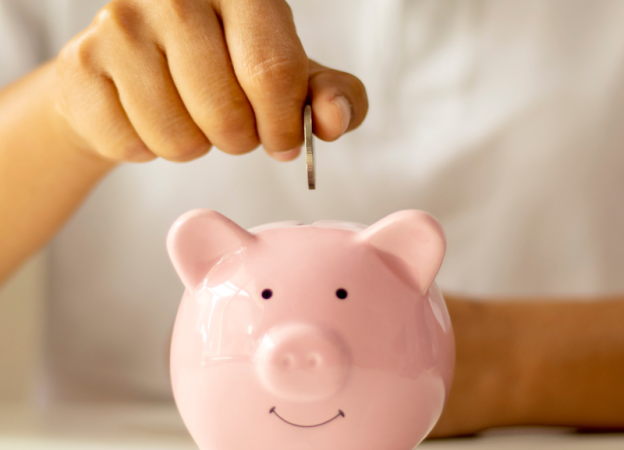 A hand places a coin in a pink piggy bank