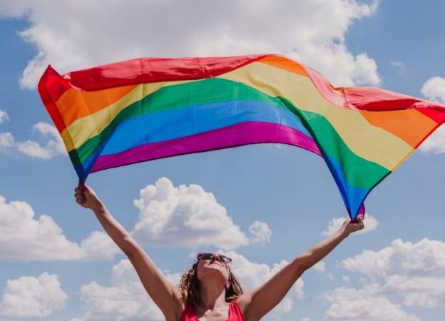 Mujer sosteniendo una bandera con los colores de la comunidad LGBT+. Woman waving an LGBT+ flag. 
