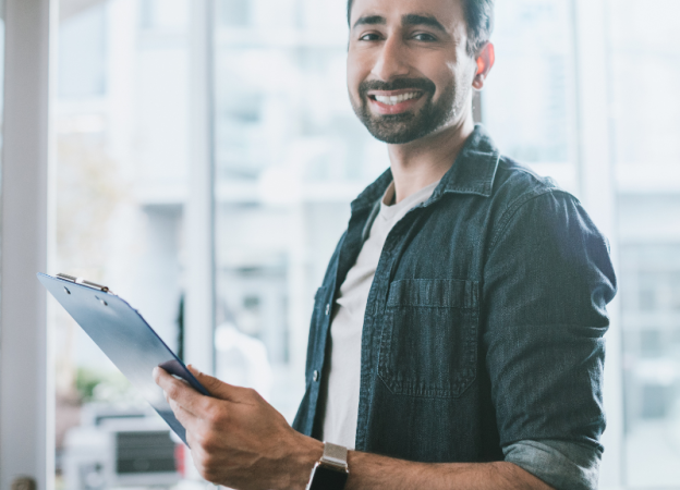 A young professional man smiles while holding a clipboard