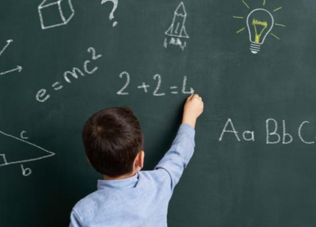 Niño de espaldas escribiendo en una pizarra, concentrado en resolver un problema matemático en clase.