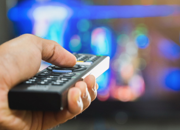 A hand holding a remote control with a blurry background of a TV