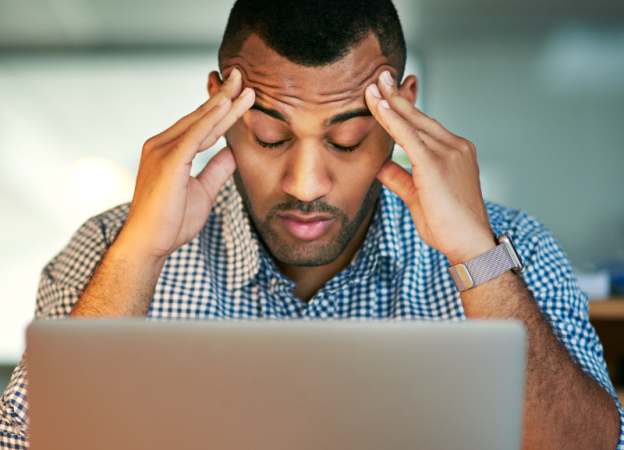 A stressed man rubs his temples while looking at his computer