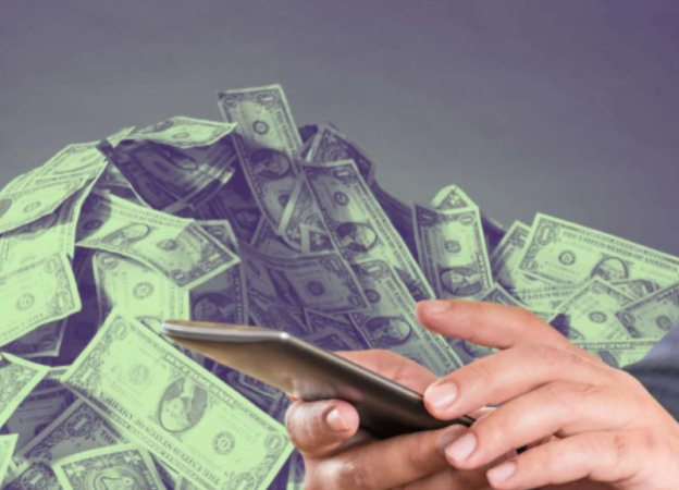 A person typing on a cell phone and a stack of cash in the background 