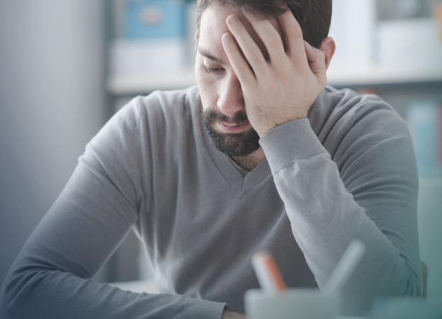 A stressed and tired man sits with his hand on his head and face