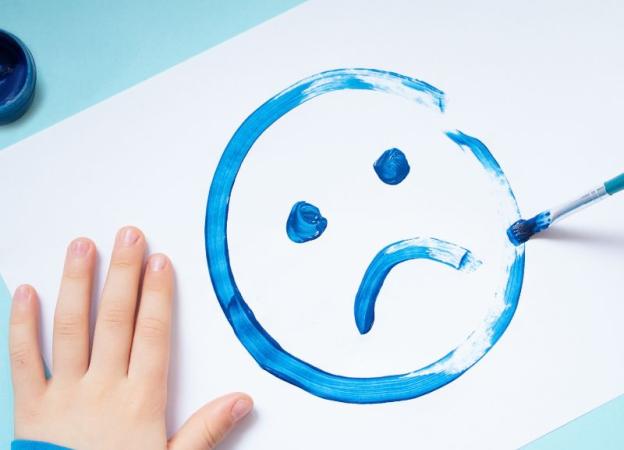 Imagen de una carita triste dibujada en tempera o acuarela por un niño. 